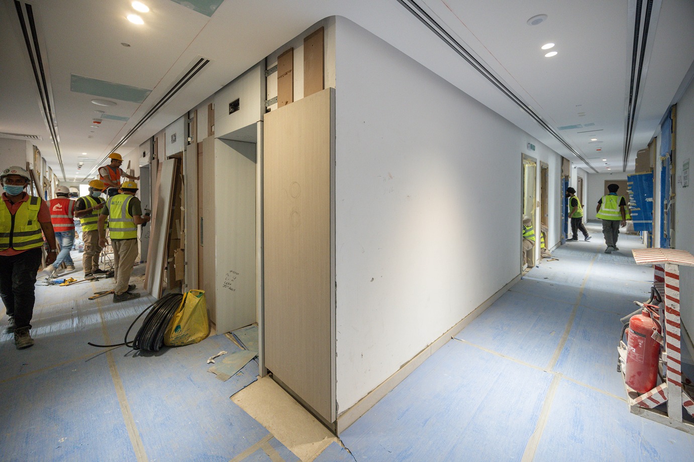 Pearl House By Imtiaz Construction workers in safety vests collaborate in a hallway under renovation, with materials and tools around.